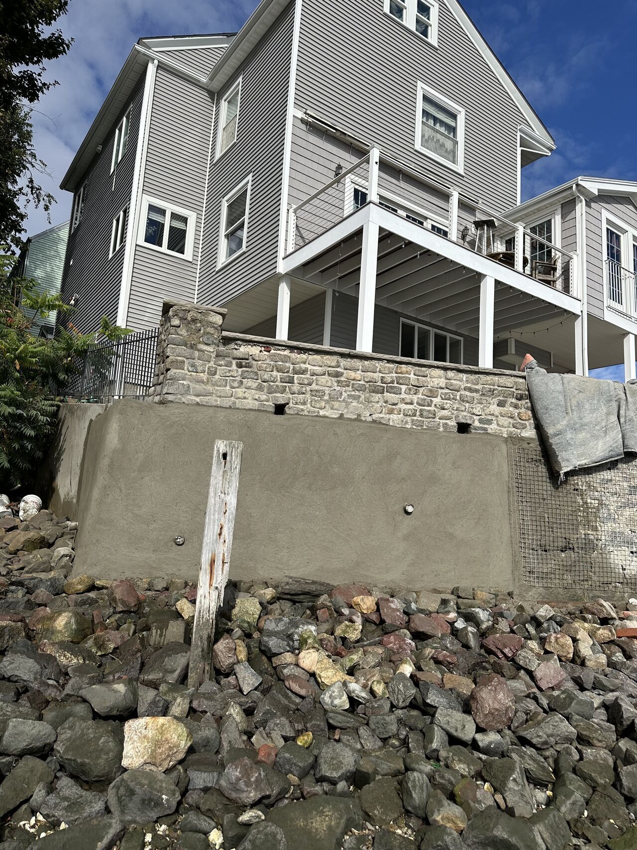 Gray house on a rocky shoreline, with a retaining wall.