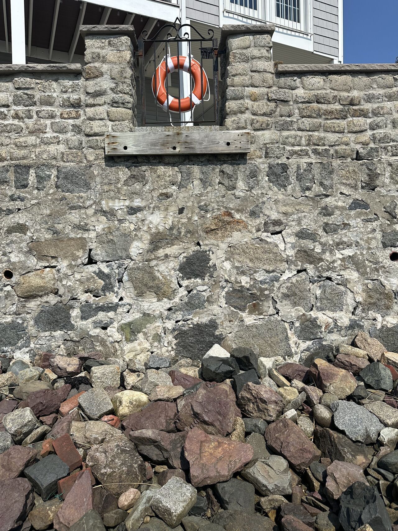 Stone wall with a life preserver and rocks at its base.