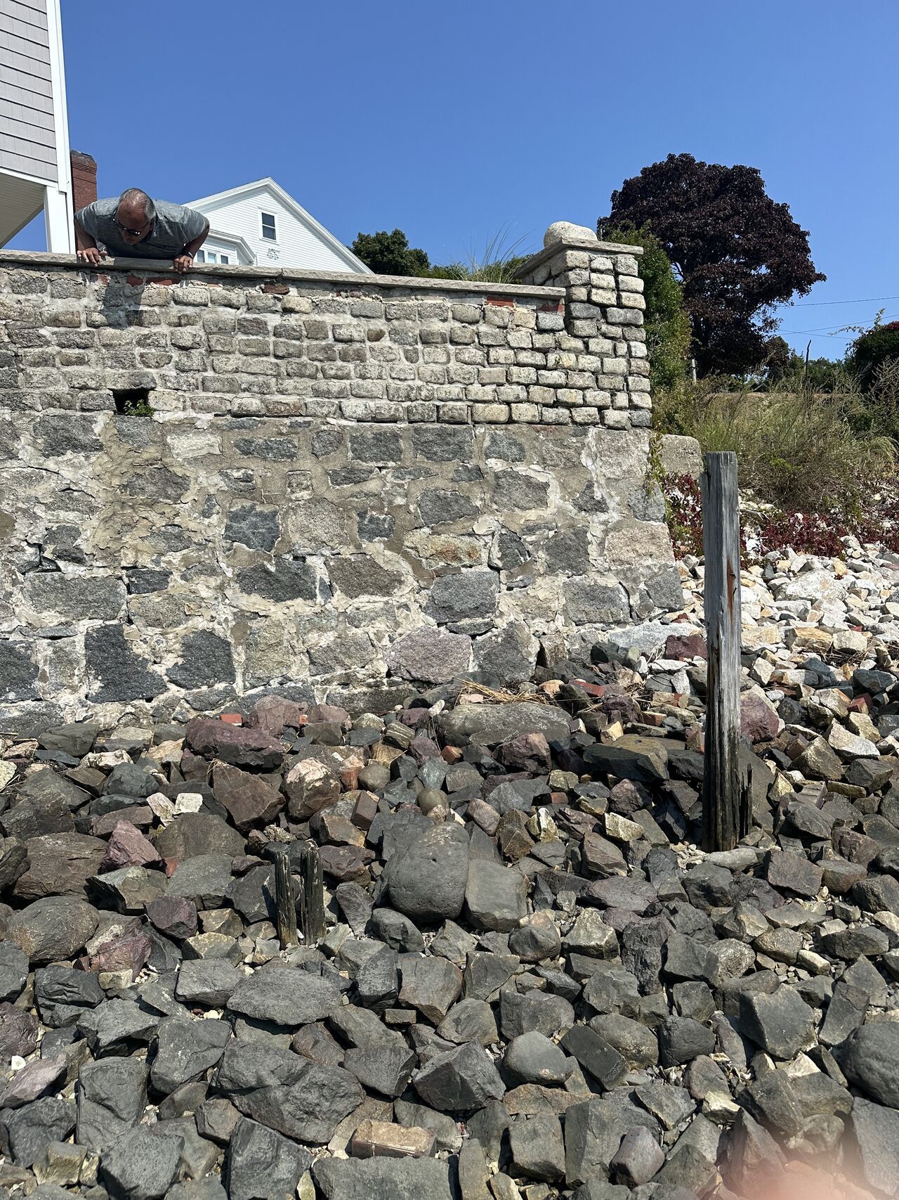 Stone wall with house in the background, a rocky shore, and a clear blue sky.