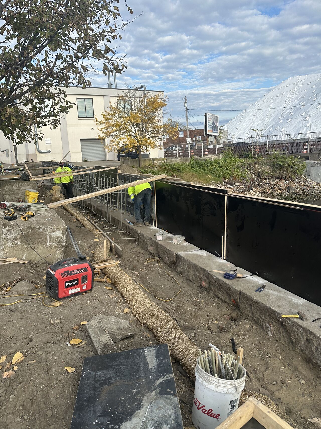 Construction workers at a site with concrete forms and black lining, working outdoors on a cloudy day.