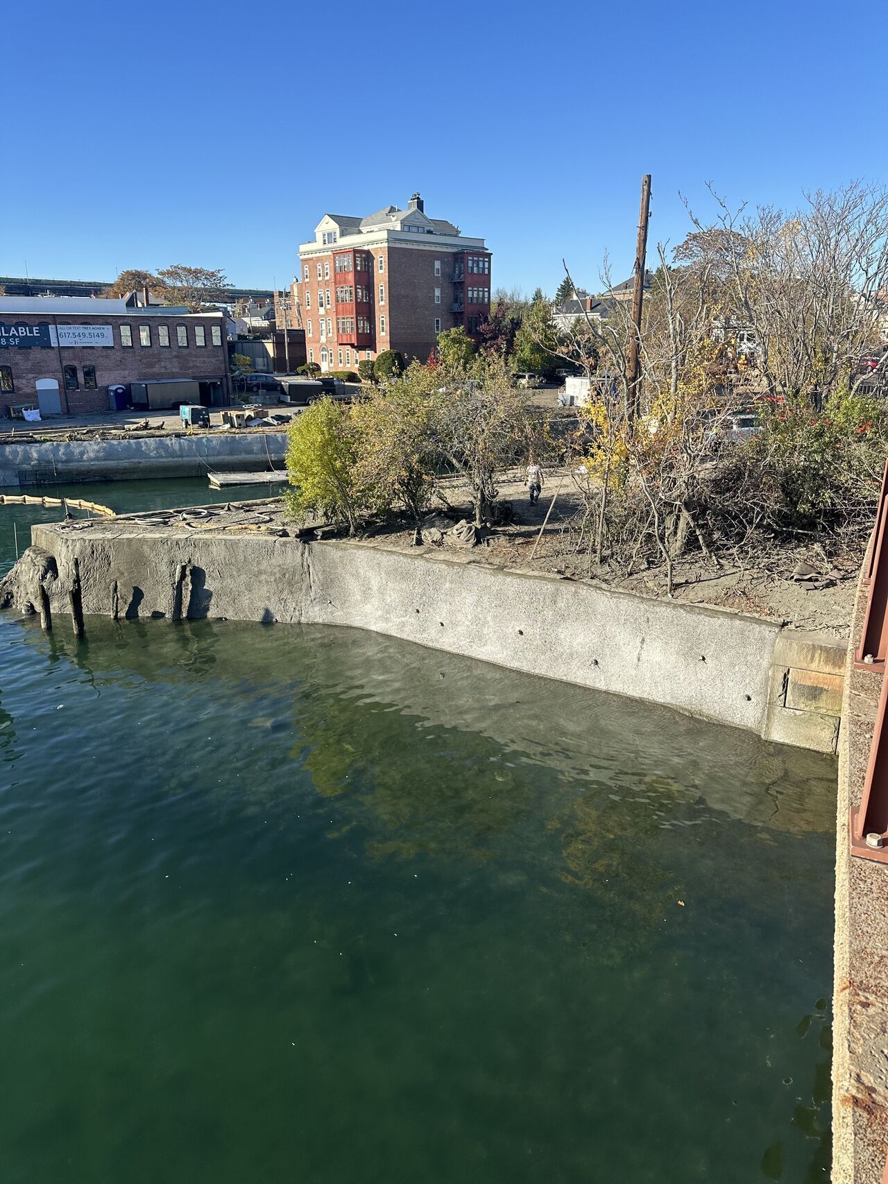 Waterfront view with concrete structures and a brick building under a clear blue sky.