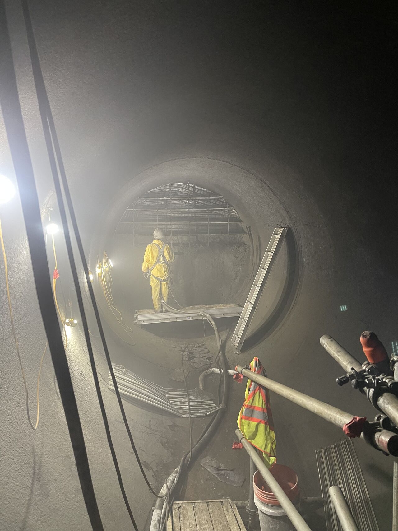Person in protective gear working inside a dark tunnel, construction in progress.