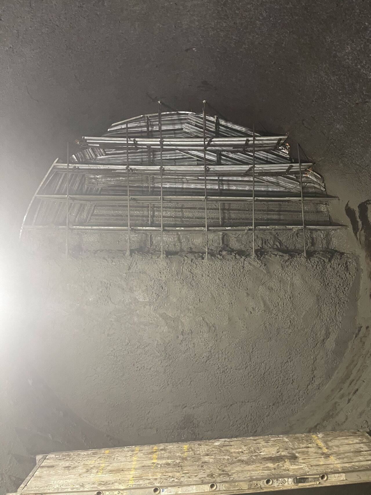 A metal structure layered above a large pile of grey debris inside a dark, round enclosure.