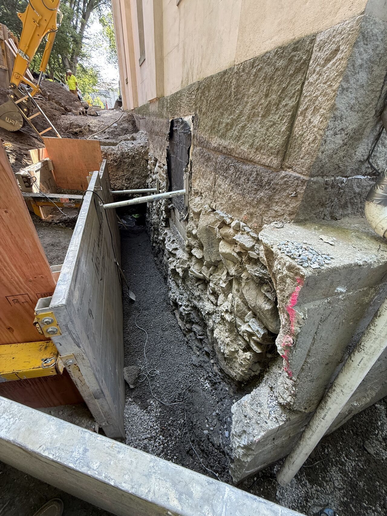 Construction site: Excavation next to a building's stone foundation. Gray gravel, wood, and concrete are visible.