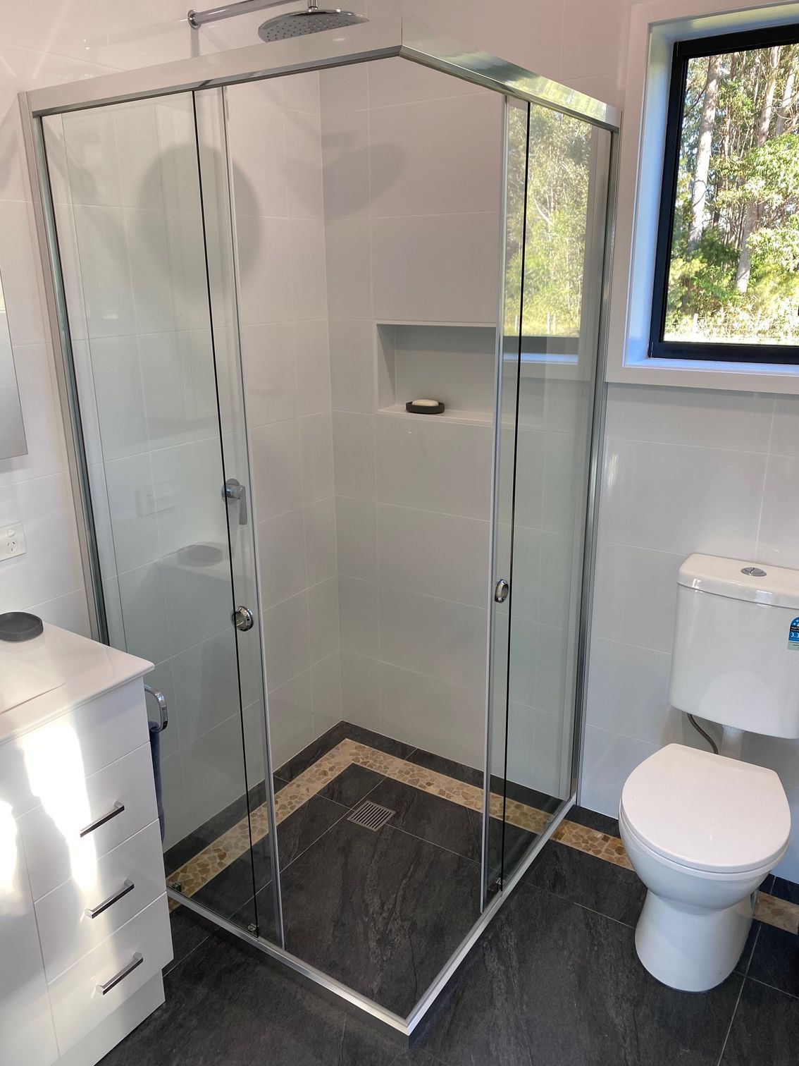 A Bathroom With a Toilet , Sink , Shower and Window — Rooney Glass in Coffs Harbour, NSW