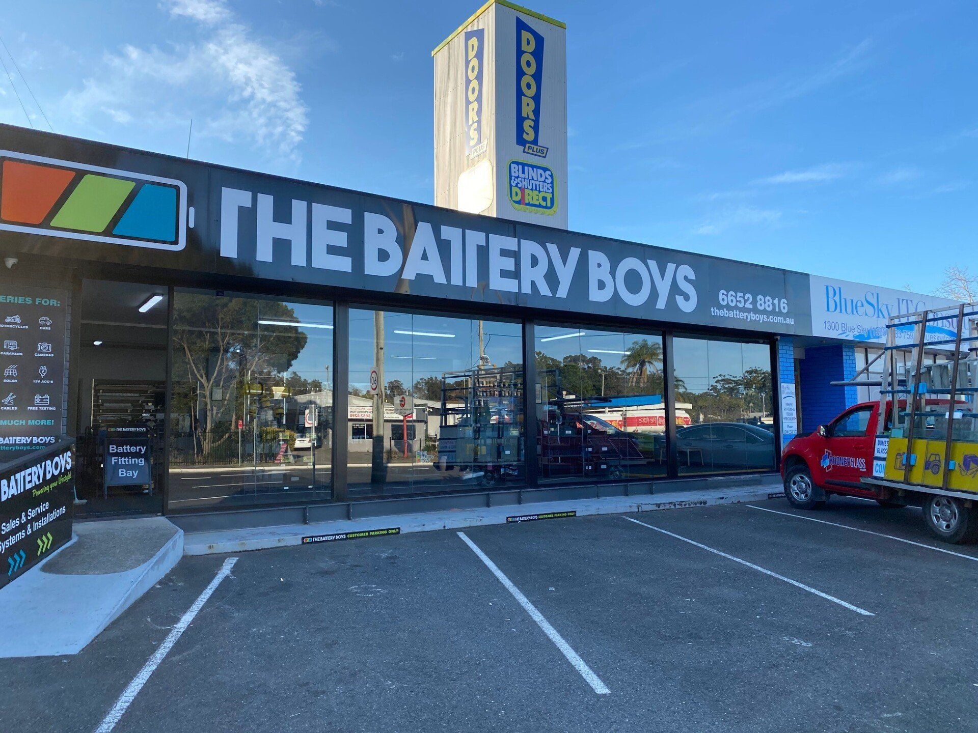 A Car is Parked in Front of a Store Called the Battery Boys — Rooney Glass in Coffs Harbour, NSW