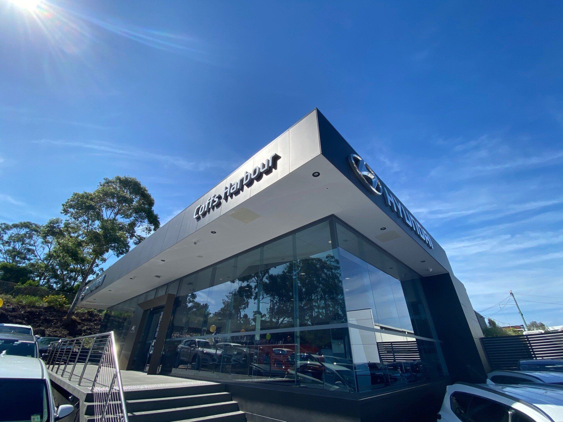 A Car Dealership With a Lot of Cars Parked in Front of It on a Sunny Day — Rooney Glass in Coffs Harbour, NSW
