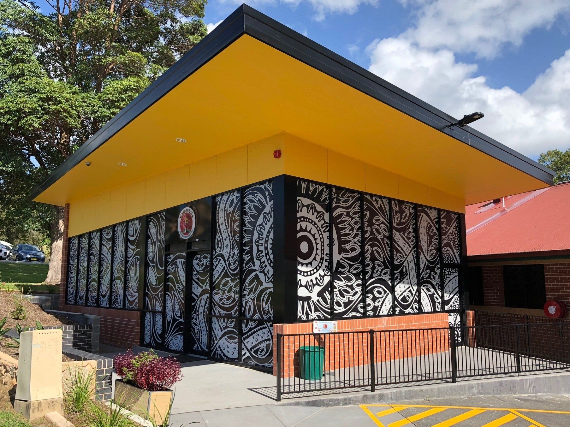 A Yellow Building With a Black Roof and a Red Roof — Rooney Glass in Coffs Harbour, NSW
