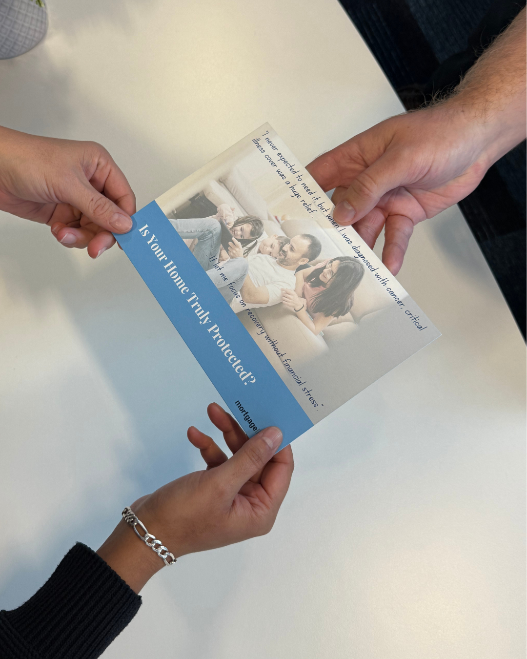 Two people exchanging a brochure with a family image. Text on the brochure: