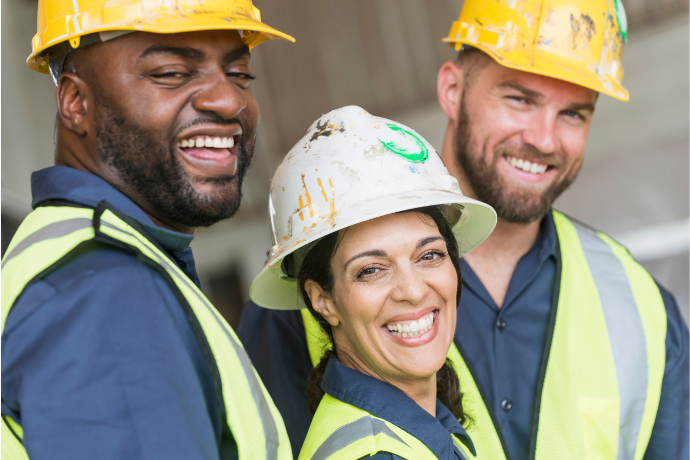 Three construction workers smiling and wearing safety vests and helmets.