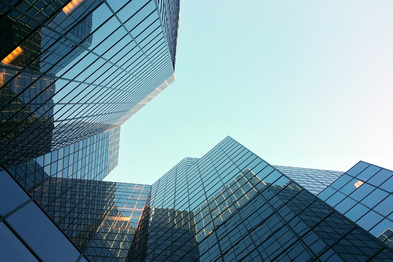 Looking up at modern glass buildings against a pale blue sky.