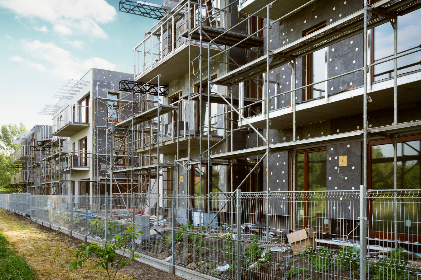 Apartment building under construction with scaffolding and fencing.