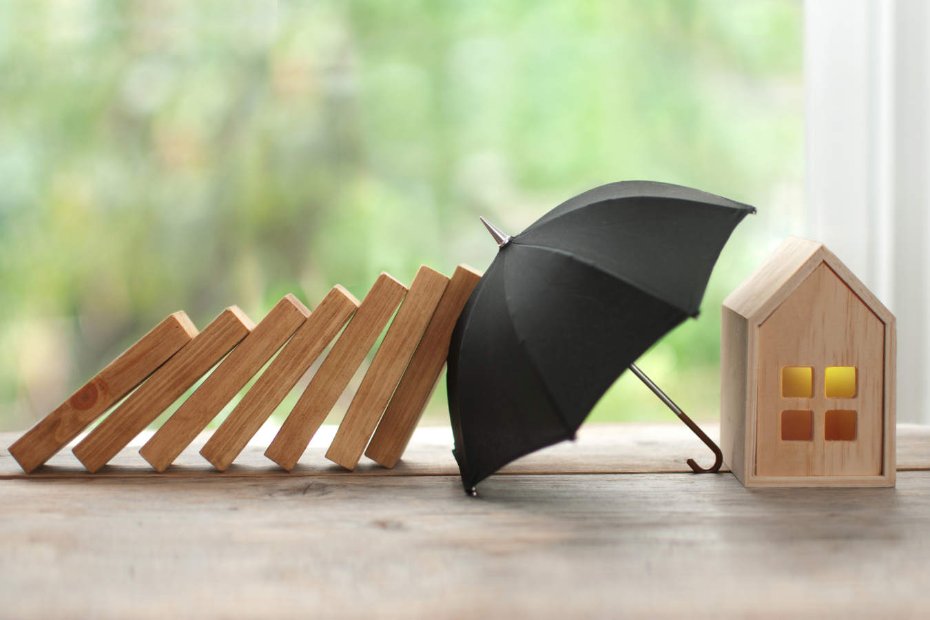An umbrella blocking falling dominoes, protecting a wooden house.