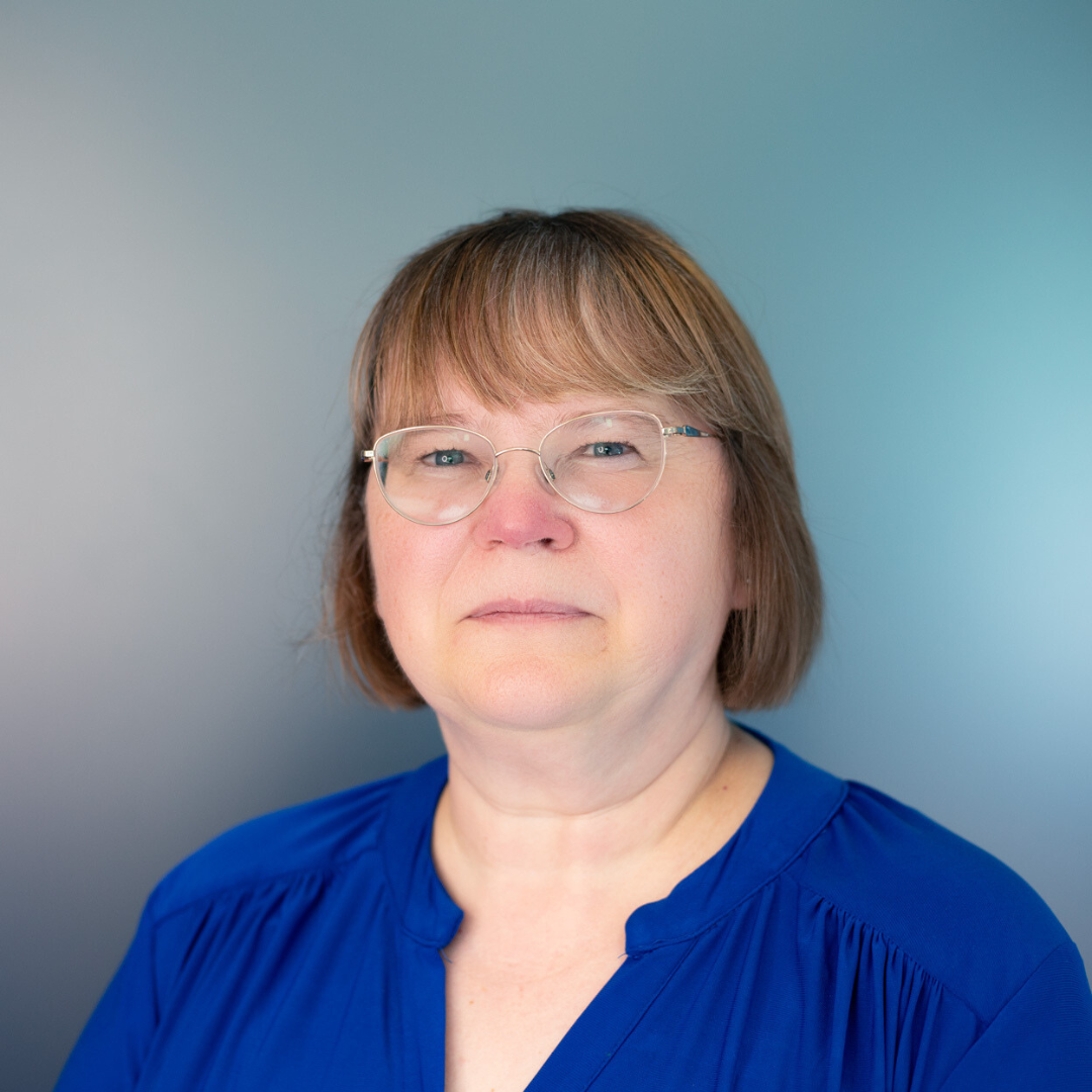 Woman with glasses and short hair in a blue shirt against a blue-grey background.