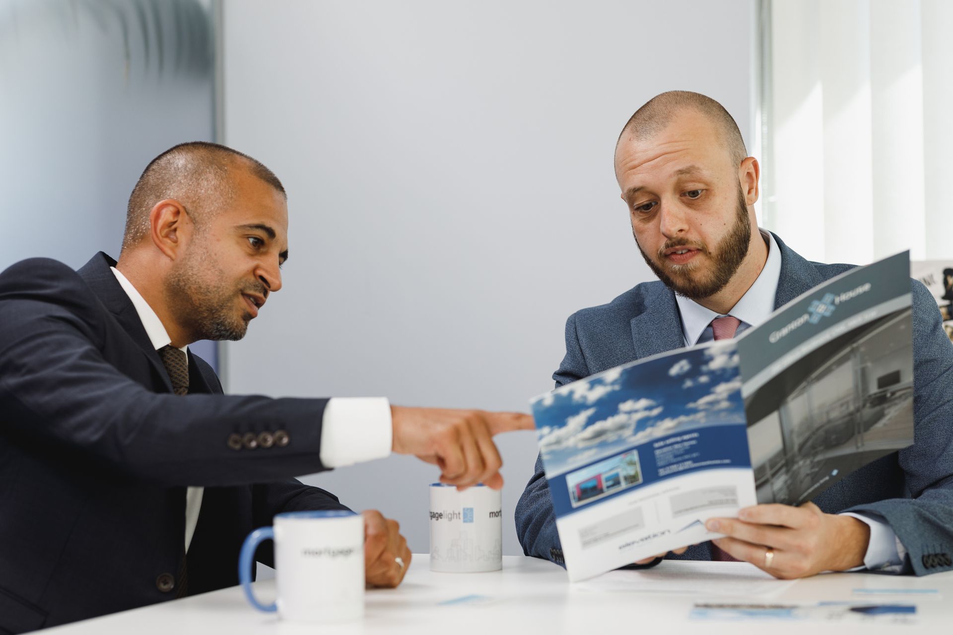 Man and woman smiling at a laptop. The man types, wearing glasses and a brown sweater. Bright, modern office setting.