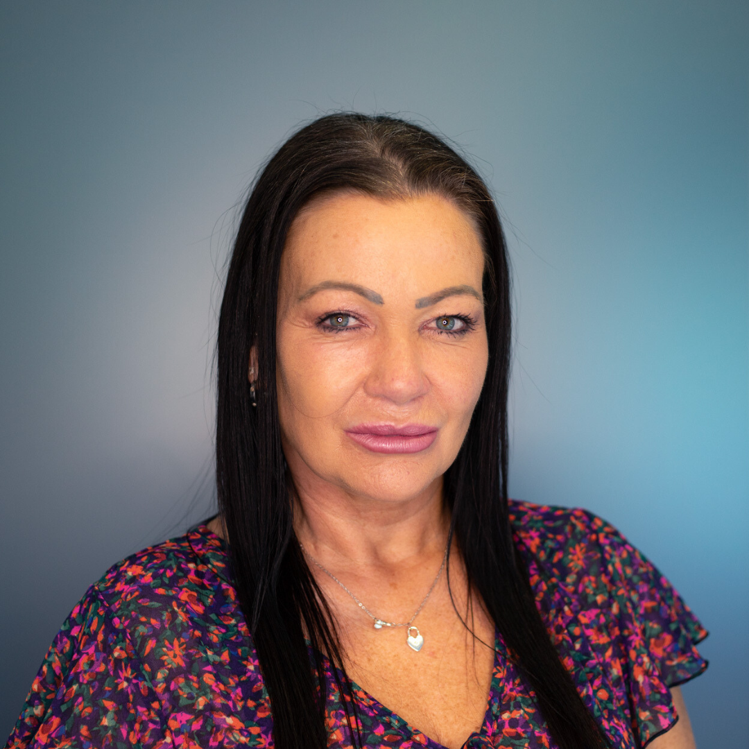 Woman with dark hair, wearing floral shirt, looking at the camera. Blue-gradient background.