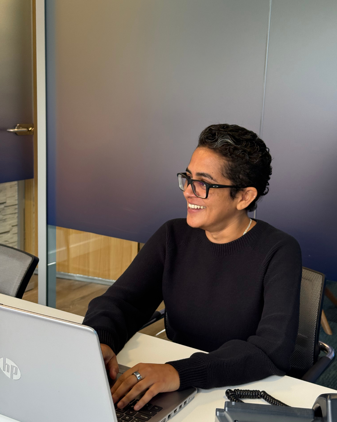 Person in beige blazer uses calculator and laptop at a desk with papers.