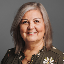 Woman with gray hair smiles, wearing a green floral top against a gray backdrop.