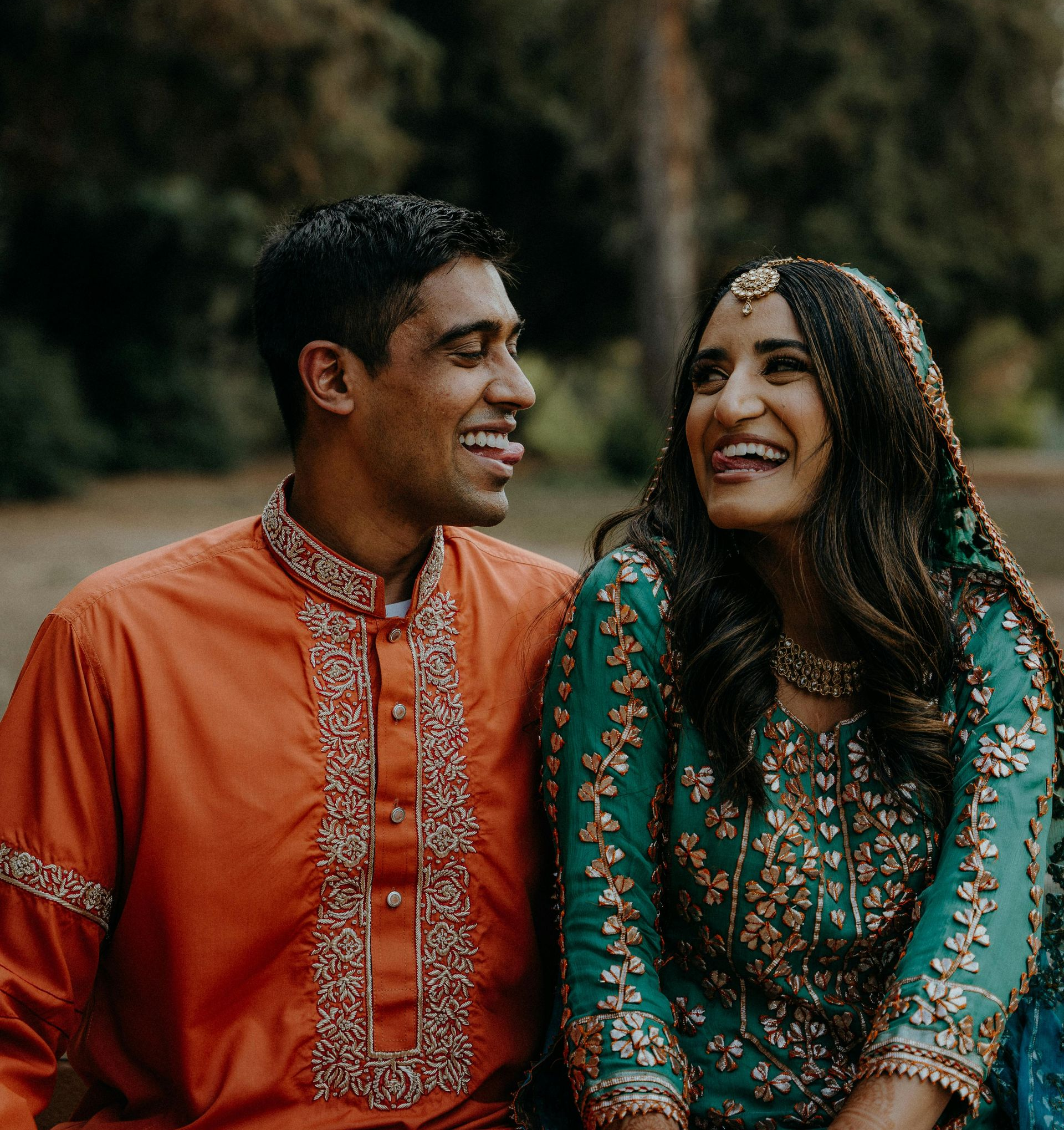 Couple in colorful traditional attire, smiling and laughing outdoors.