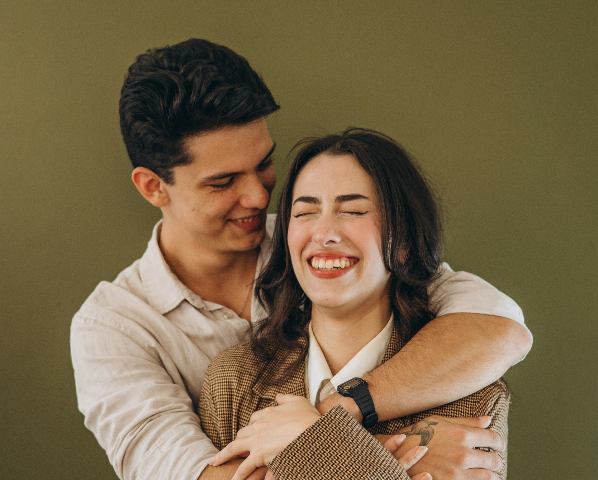 Man hugging smiling woman, both against a green backdrop.