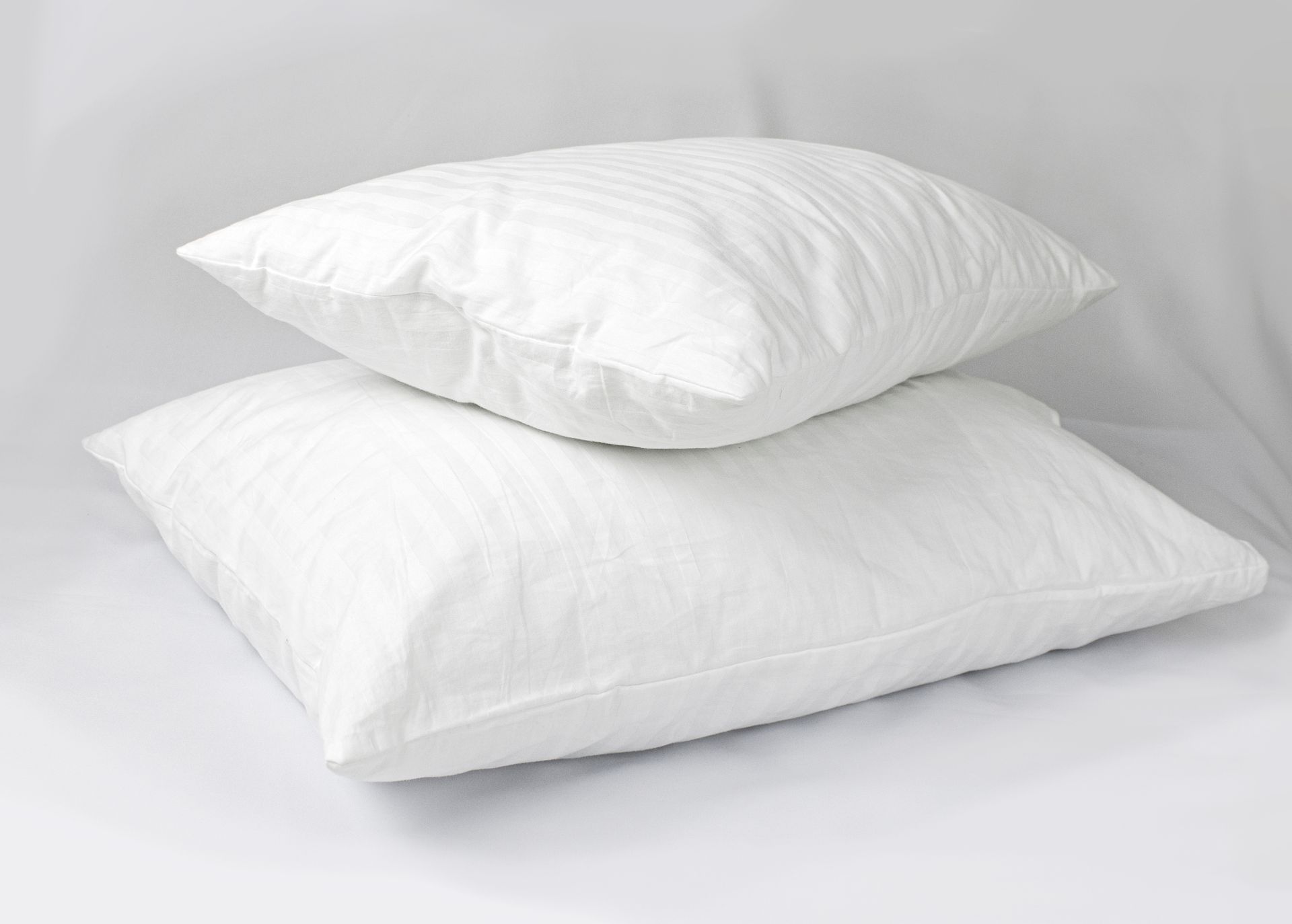Two white pillows are stacked on top of each other on a bed.