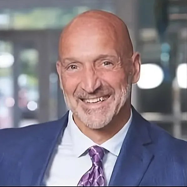 A bald man in a suit and tie is smiling for the camera.