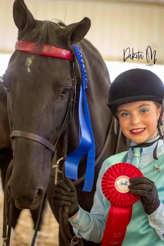 photo of Lenux Stables academy rider holding horse and displaying her winning and reserve ribbons after horse show class