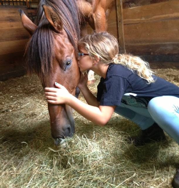 photo of girl kissing horse on side of head while in stall