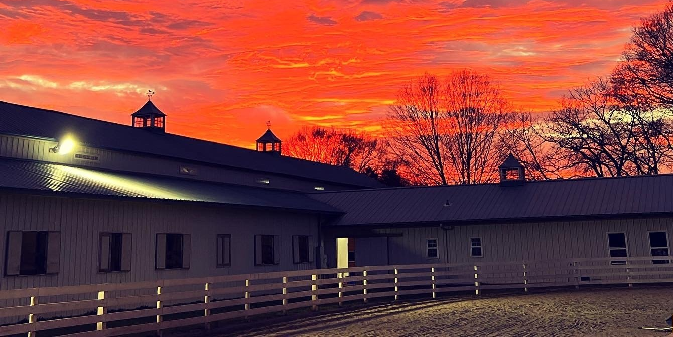 photo of Lenux Stables outdoor ring and barn with beautiful sunset in background