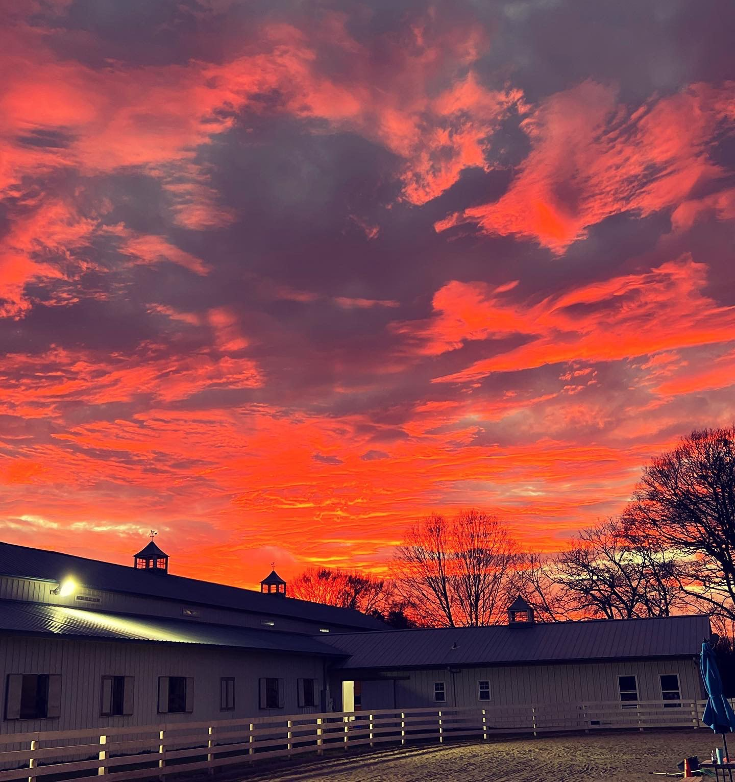 photo of Lenux Stables main barn and outdoor riding arena, with beautiful fiery sunset in background