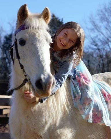 photo of girl sitting on and hugging white pony