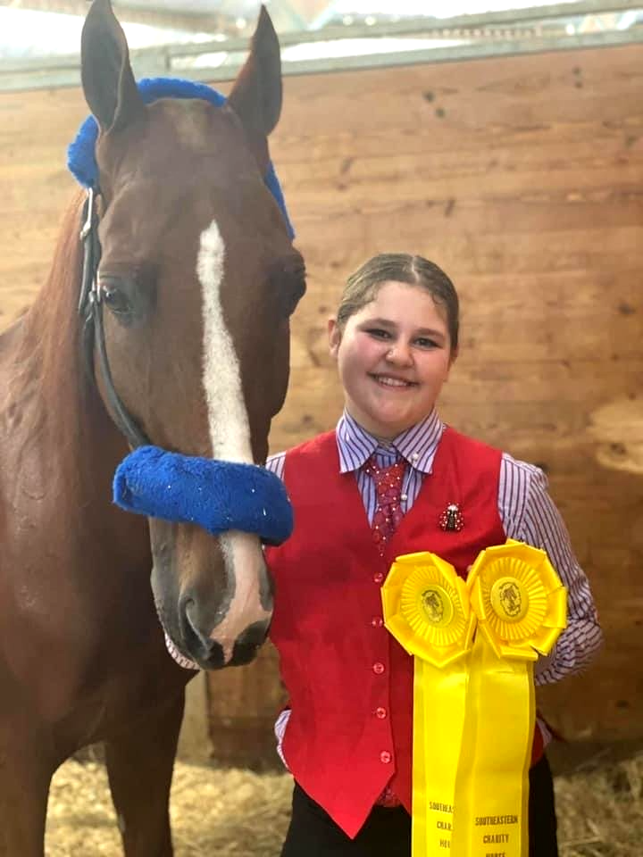 photo of Lenux Stables academy rider holding horse and displaying her ribbons at horse show