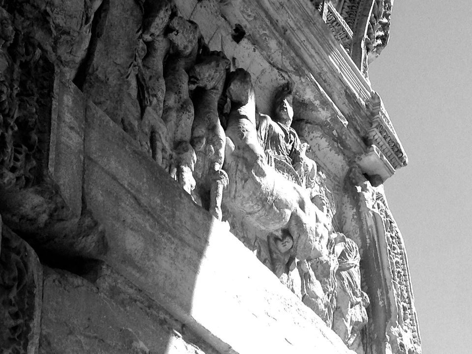 Una foto in bianco e nero, scattata dal basso, di sculture in pietra a rilievo, consumate dal tempo, con figure scolpite, sulla facciata riccamente decorata di un edificio.