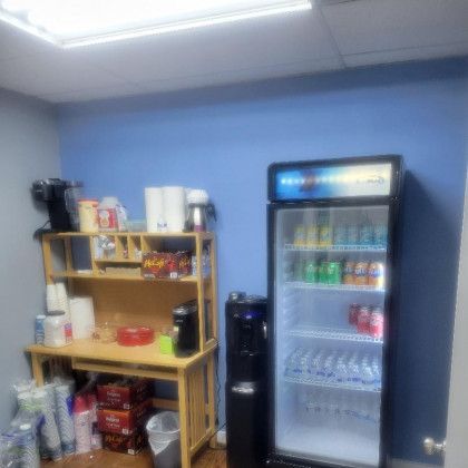 A room with a desk, refrigerator, and water cooler.