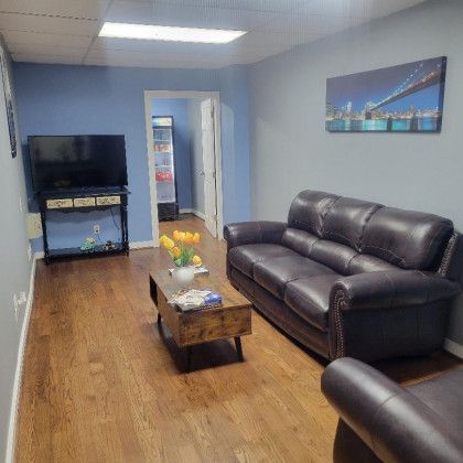 A waiting room with a couch, chair, coffee table and television.