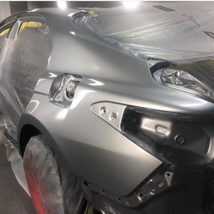 A silver car is being painted in a garage.