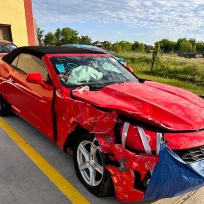 A red car with a damaged front end is parked in a parking lot.