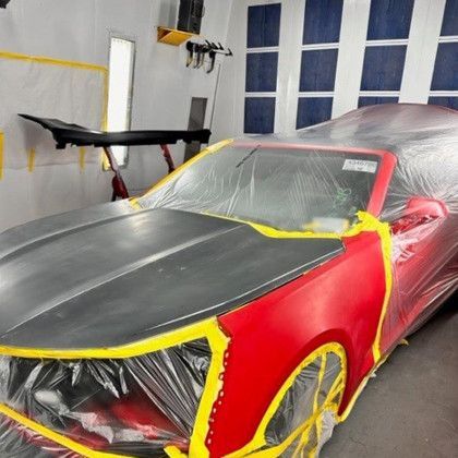 A red car is being painted in a paint booth