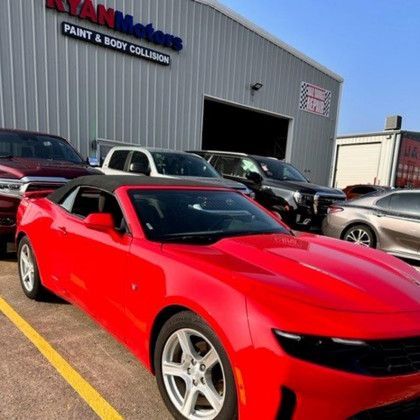 A red car is parked in a parking lot in front of a building.