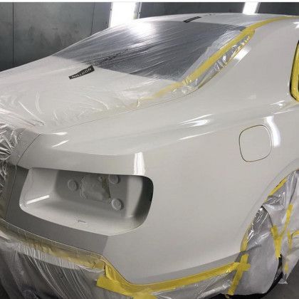 A white car is wrapped in plastic and tape in a garage.