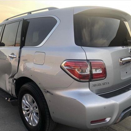 A silver suv with a damaged side is parked on the side of the road.