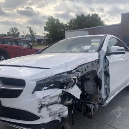 A white car with a damaged front end is parked in a parking lot.