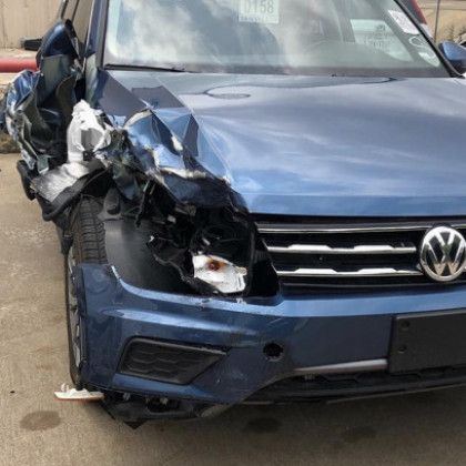 A blue volkswagen with a damaged front end is parked in a parking lot.