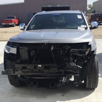 A silver jeep with a damaged front end is parked in a parking lot.
