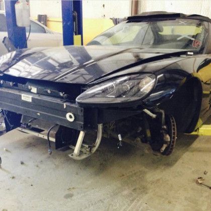 A black car with a broken bumper is sitting in a garage.