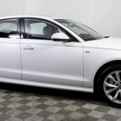 A white car is parked in a garage with a checkered floor.