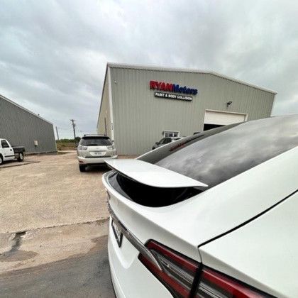 A white car is parked in front of a building that says ryan motors.