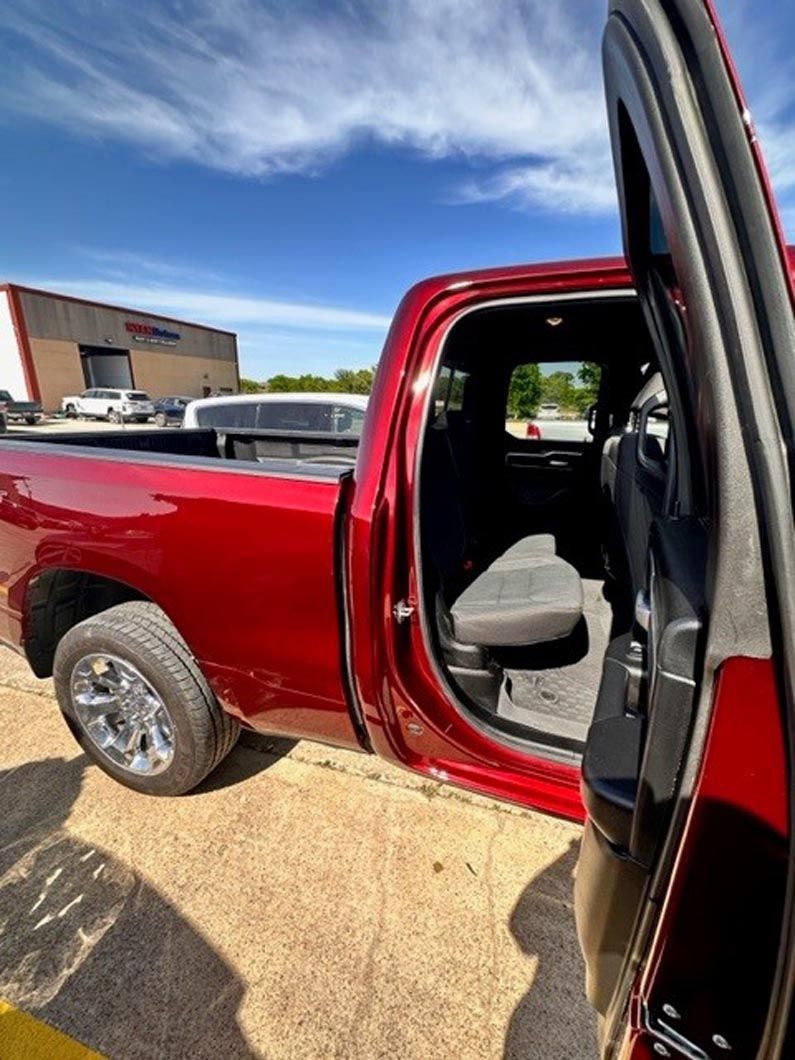 A red truck is parked in a parking lot with the door open.
