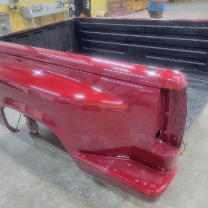 A red truck bed is sitting on the ground in a garage.