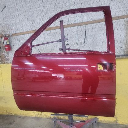 A red truck door is sitting on a lift in a garage.